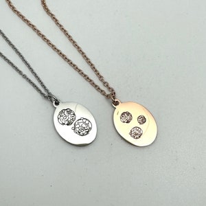 Può includere: Due collane d'argento con ciondoli ovali. Un ciondolo presenta un design di tre piccoli cerchi, l'altro un design di due cerchi più grandi. La collana a sinistra è d'argento, quella a destra è oro rosa.