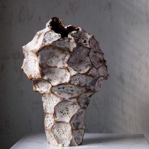 May include: A sculptural ceramic vase with a highly textured, porous surface featuring a honeycomb-like pattern. The exterior displays a mottled grey and white finish with deep brown, metallic-toned crevices defining each individual cell-like section.