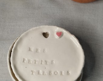 Może przedstawiać: Biała ceramiczna miseczka z podwyższonym brzegiem i małym różowym sercem w środku. Miseczka ma napis "LES PETITS TRÉSORS" wygrawerowany na powierzchni.