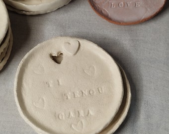 Może przedstawiać: Dwa białe ceramiczne podkładki pod kubki z wypukłymi sercami i napisem "I  TIENGO  GANAS" na górnej podkładce.