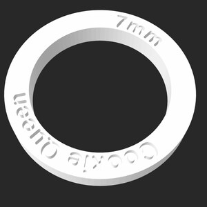 Puede incluir: Anillo de plástico blanco con el texto "Cookie Queen" y "7 mm" inscrito en él.