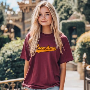 May include: A maroon t-shirt with a yellow vintage-style graphic that says "Crenshaw" on the front.