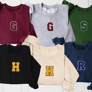 May include: Five crewneck sweatshirts in different colors with a large letter embroidered on the front. The letters are G, G, S, H, and R. The sweatshirts are maroon, gray, green, black, and navy blue.