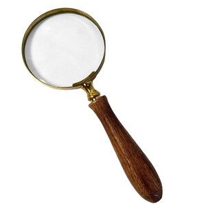 May include: A magnifying glass with a clear lens and a brass-colored frame. The handle is made of polished wood. The magnifying glass is designed for reading or examining small objects.