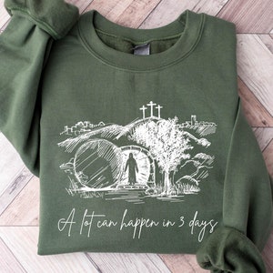 May include: A green sweatshirt with a white graphic of a tomb, a figure walking away from it, and the text "A lot can happen in 3 days".