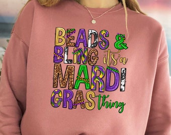 May include: A pink sweatshirt with the text "Beads & Bling it's a Mardi Gras thing" in green, purple, and gold lettering.