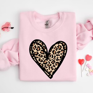 May include: A pink sweatshirt with a black outlined heart design featuring a leopard print pattern.