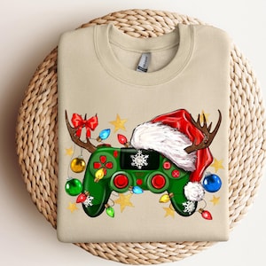 May include: A beige sweatshirt with a green video game controller decorated with Christmas ornaments, a Santa hat, and reindeer antlers.