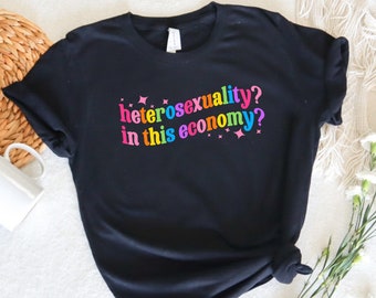 May include: Black t-shirt with the text "heterosexuality? in this economy?" in rainbow colors.