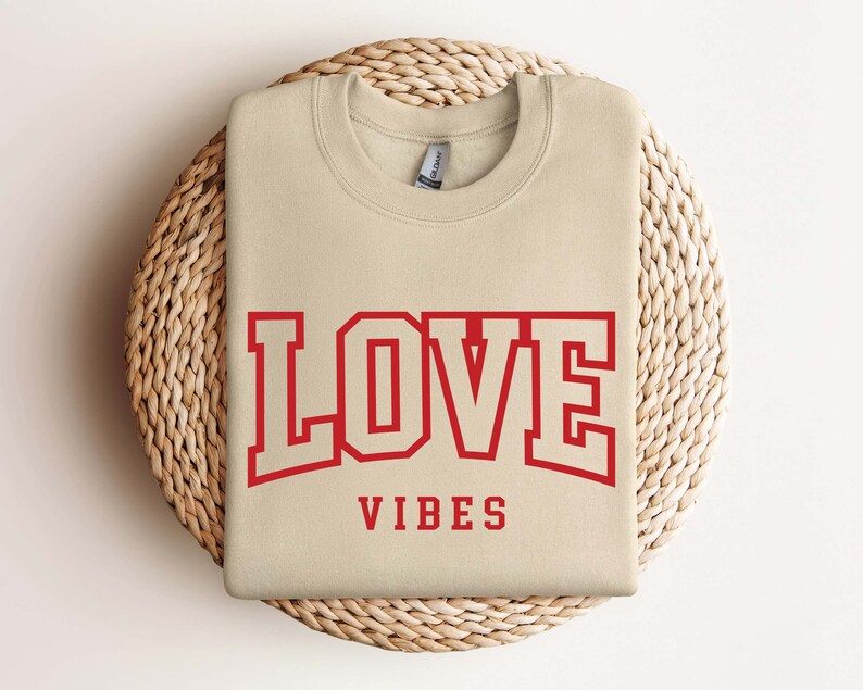 May include: A beige sweatshirt with the text "LOVE VIBES" in red lettering. The word "LOVE" is in a large, bold font with a red outline.