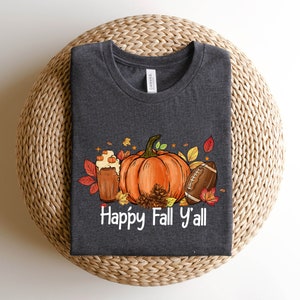May include: A dark gray t-shirt with a graphic design of a pumpkin, football, and a fall-themed drink. The text "Happy Fall Y'all" is printed below the graphic.