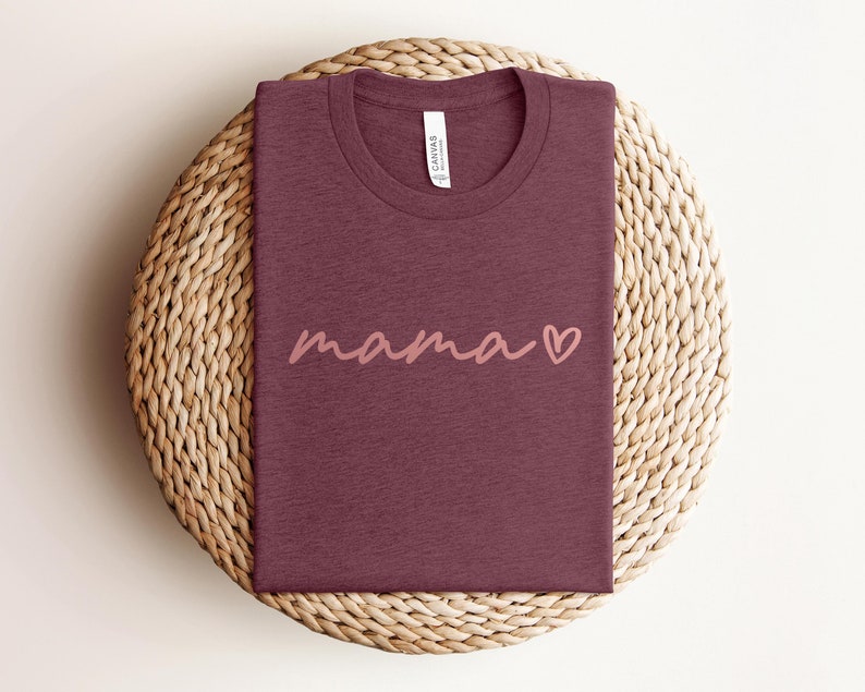 May include: A maroon t-shirt with the word "mama" written in pink script with a pink heart next to it.