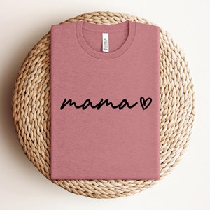 May include: A pink t-shirt with the word "mama" written in black cursive with a small heart next to it.