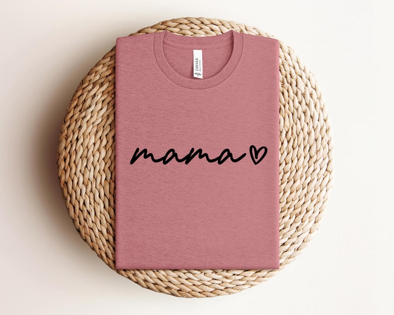 May include: A pink t-shirt with the word "mama" written in black cursive with a small heart next to it.