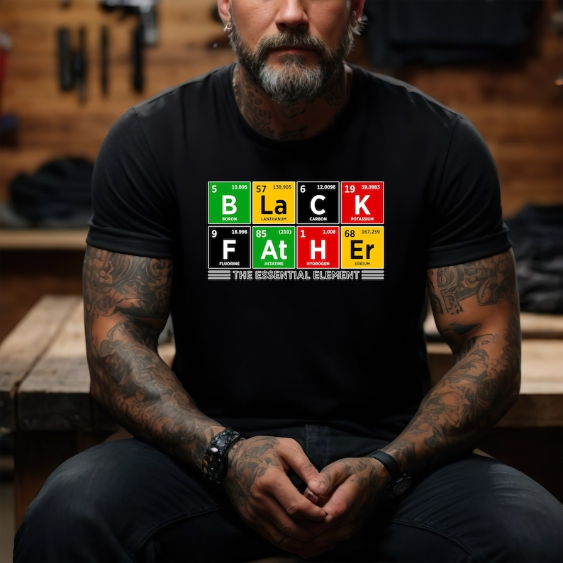 Op de afbeelding: Zwart T-shirt met een afbeelding van het periodiek systeem van de elementen die "Black Father" spellen met de tagline "het essenti&euml;le element".