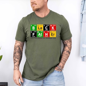 Op de afbeelding: Een groen T-shirt met een afbeelding van het periodiek systeem van de elementen die "Black Father" spellen met de tekst "The Essential Element" eronder.