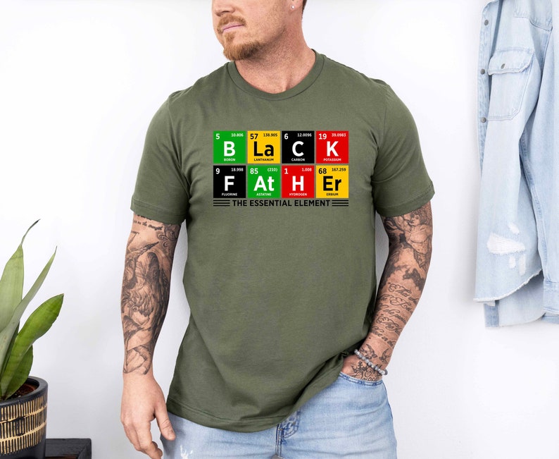 Op de afbeelding: Een groen T-shirt met een afbeelding van het periodiek systeem van de elementen die "Black Father" spellen met de tekst "The Essential Element" eronder.