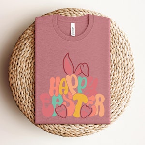 May include: A pink t-shirt with a colorful graphic of a bunny rabbit and the text "Happy Easter".