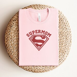 May include: Pink t-shirt with a red Superman logo and the text "Supermom" above it.