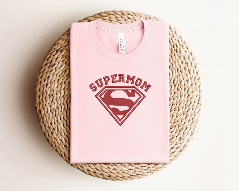 May include: Pink t-shirt with a red Superman logo and the text "Supermom" above it.
