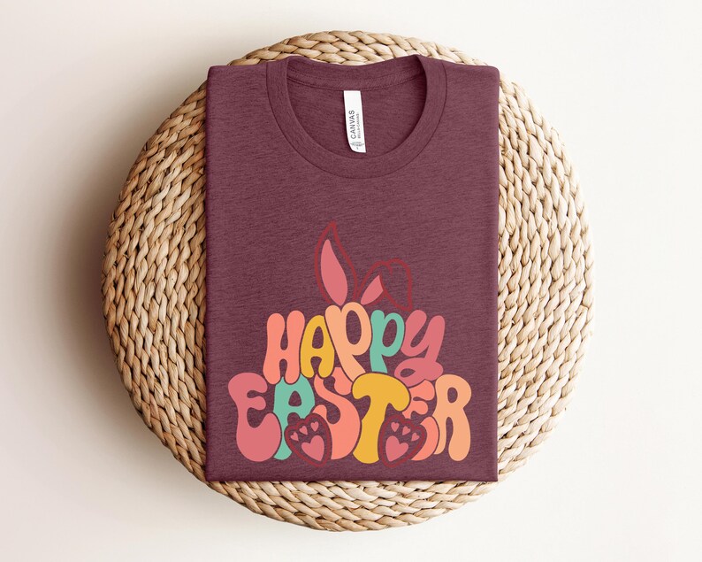 May include: A maroon t-shirt with a retro-style graphic that says "Happy Easter" in colorful letters. The graphic features a bunny rabbit with floppy ears.
