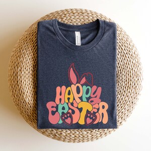 May include: A dark gray t-shirt with a colorful graphic design that says "Happy Easter" with bunny ears. The graphic is in a retro style with a rainbow color scheme.