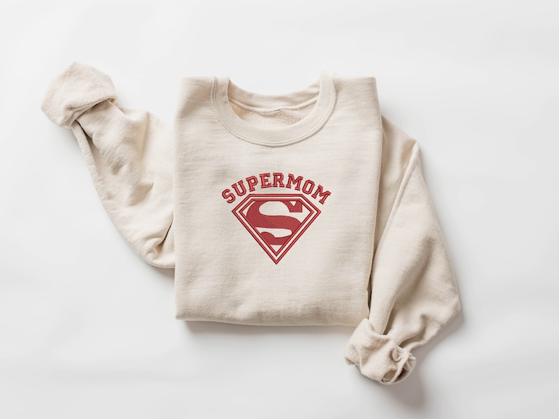 May include: A beige sweatshirt with a red Superman logo and the text "SUPERMOM" printed on the front.