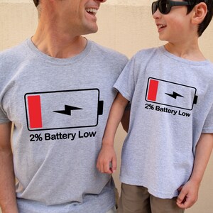 May include: Two people wearing gray t-shirts with a black and red battery icon and the text "2% Battery Low".