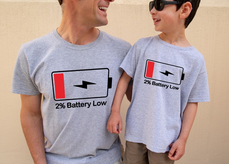 May include: Two people wearing gray t-shirts with a black and red battery icon and the text "2% Battery Low".
