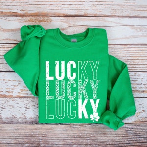 May include: Green sweatshirt with the word "LUCKY" repeated three times in white, with a distressed, vintage look. The word "LUCKY" is stacked vertically, with a shamrock at the bottom.