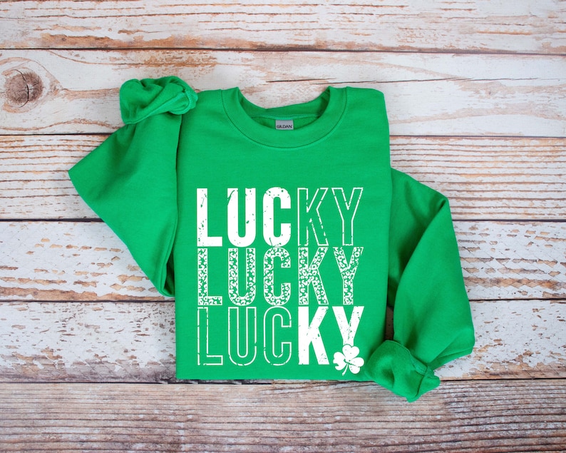 May include: Green sweatshirt with the word "LUCKY" repeated three times in white, with a distressed, vintage look. The word "LUCKY" is stacked vertically, with a shamrock at the bottom.