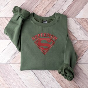 May include: Green sweatshirt with a red Superman logo and the text "SUPERMOM" above it.