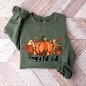 May include: Green sweatshirt with a graphic of a pumpkin, a glass of pumpkin spice, a football, and fall leaves. The text "Happy Fall y'all" is printed below the graphic.