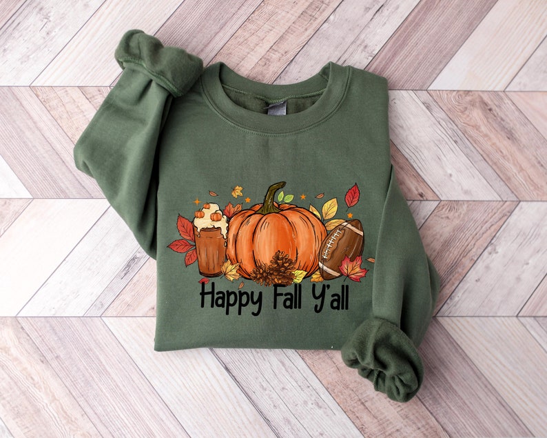 May include: Green sweatshirt with a graphic of a pumpkin, a glass of pumpkin spice, a football, and fall leaves. The text "Happy Fall y'all" is printed below the graphic.