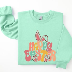 May include: A light green sweatshirt with a colorful "Happy Easter" graphic featuring bunny ears and paw prints.