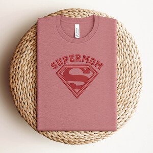 May include: A pink t-shirt with the text "SUPERMOM" and a red Superman logo.