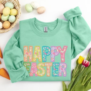 May include: A mint green sweatshirt with the words "Happy Easter" in colorful letters made up of small bunny and flower designs.