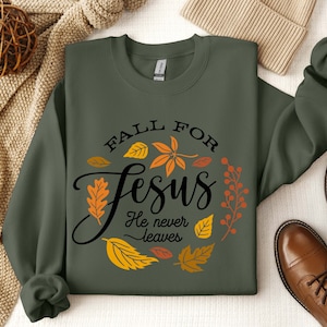 May include: A green sweatshirt with the text "Fall for Jesus He never leaves" in black lettering. The text is surrounded by a wreath of orange, yellow, and red leaves.