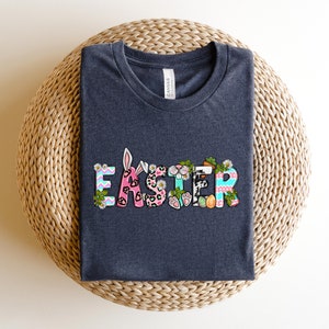 May include: A dark gray t-shirt with the word "Easter" printed on the front. The letters are decorated with colorful patterns, including animal print, stripes, and polka dots.
