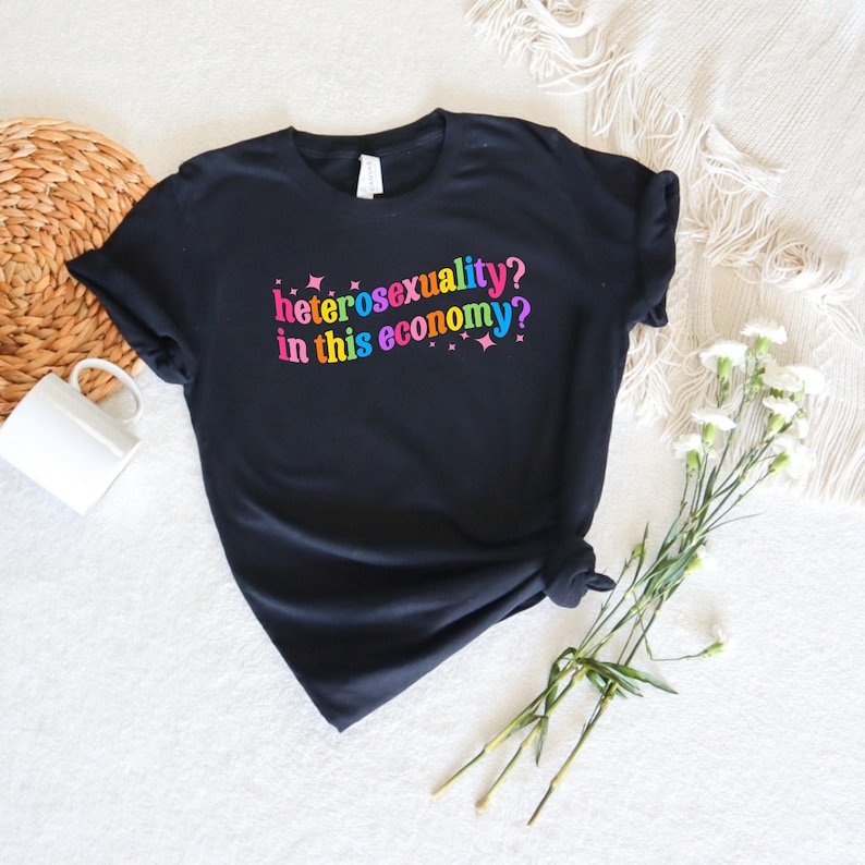 May include: Black t-shirt with the text "heterosexuality? in this economy?" in rainbow colors.