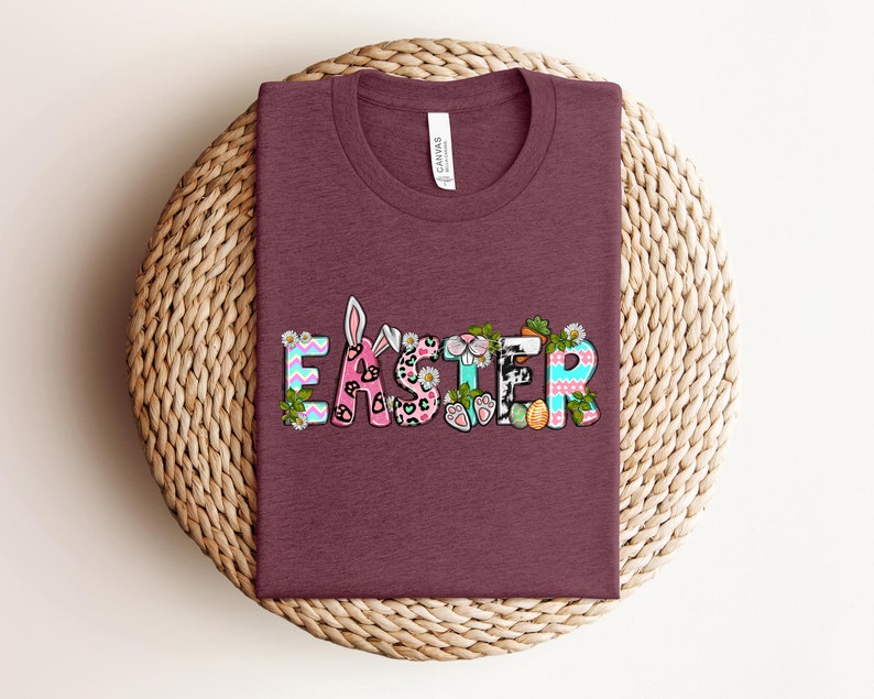 May include: A maroon t-shirt with the word "Easter" in colorful letters decorated with bunny ears, flowers, and other Easter-themed designs.