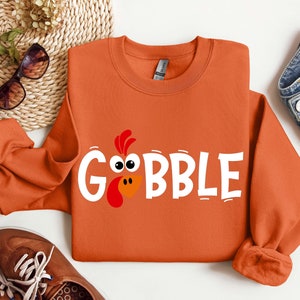 May include: Orange sweatshirt with a white graphic of a turkey head and the word "GOBBLE".