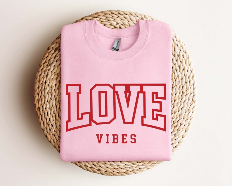 May include: Pink sweatshirt with the text "LOVE VIBES" in red block letters.