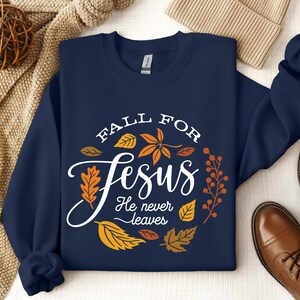 May include: Navy blue sweatshirt with a white circle design featuring the text "Fall for Jesus He never leaves" surrounded by orange and yellow leaves.