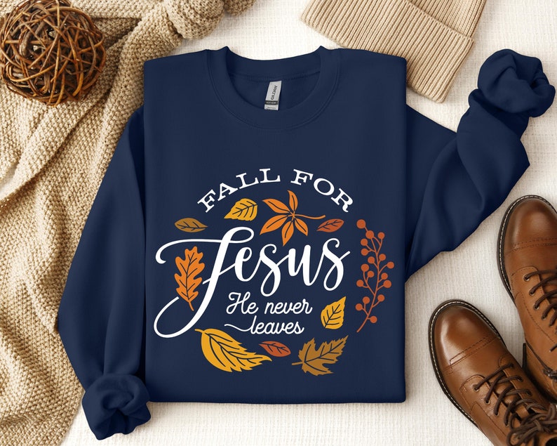May include: Navy blue sweatshirt with a white circle design featuring the text "Fall for Jesus He never leaves" surrounded by orange and yellow leaves.