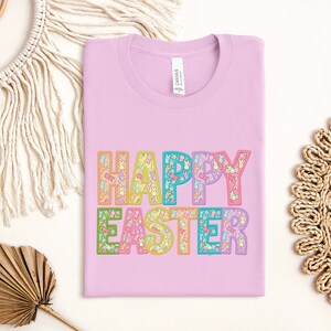 May include: A pink t-shirt with the text "HAPPY EASTER" in rainbow colors. The letters are filled with small Easter-themed illustrations.