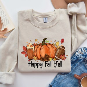 May include: A beige sweatshirt with a graphic design of a pumpkin, a football, and a glass of fall beverage. The text "Happy Fall Y'all" is printed below the graphic.