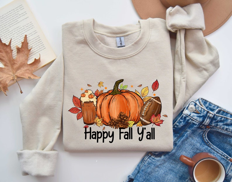 May include: A beige sweatshirt with a graphic design of a pumpkin, a football, and a glass of fall beverage. The text "Happy Fall Y'all" is printed below the graphic.