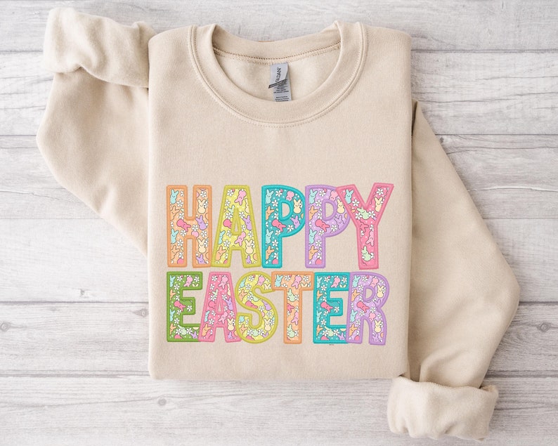 May include: A beige sweatshirt with the words "Happy Easter" printed on the front. The letters are outlined in different colors and filled with a pattern of pastel bunnies and flowers.