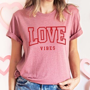 May include: A pink t-shirt with the text "LOVE VIBES" in red block letters.